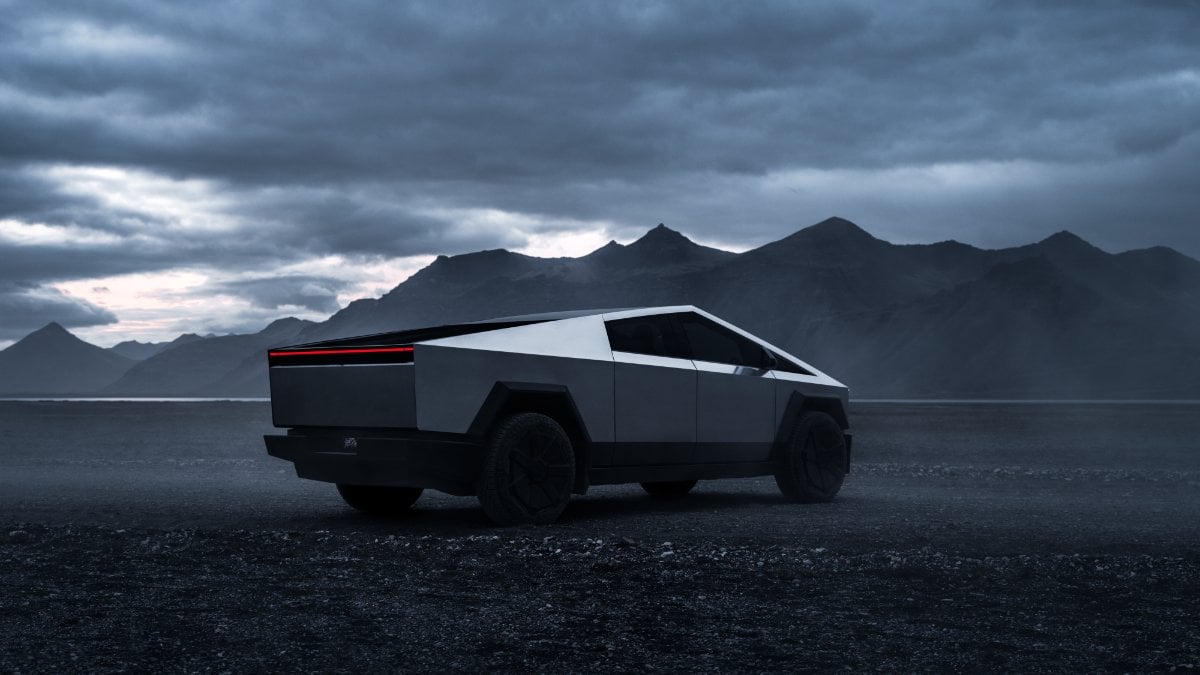 A Tesla Cybertruck parked on a rugged landscape, silhouetted against dramatic mountains and an overcast sky.