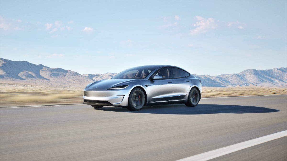 Silver Tesla Model 3 driving on desert highway with mountain range in background, dynamic motion shot