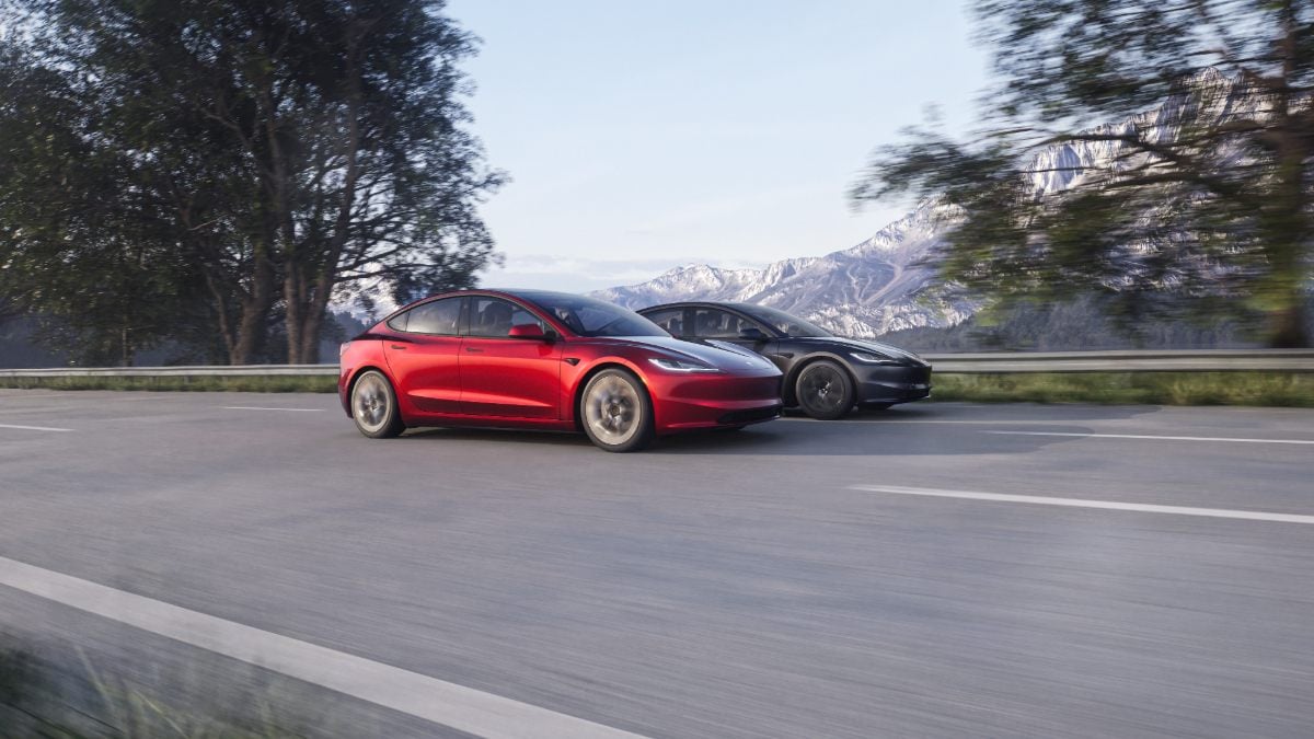 Two Tesla Model 3 sedans, one red and one black, driving on a mountain road with snow-capped peaks visible in the background.