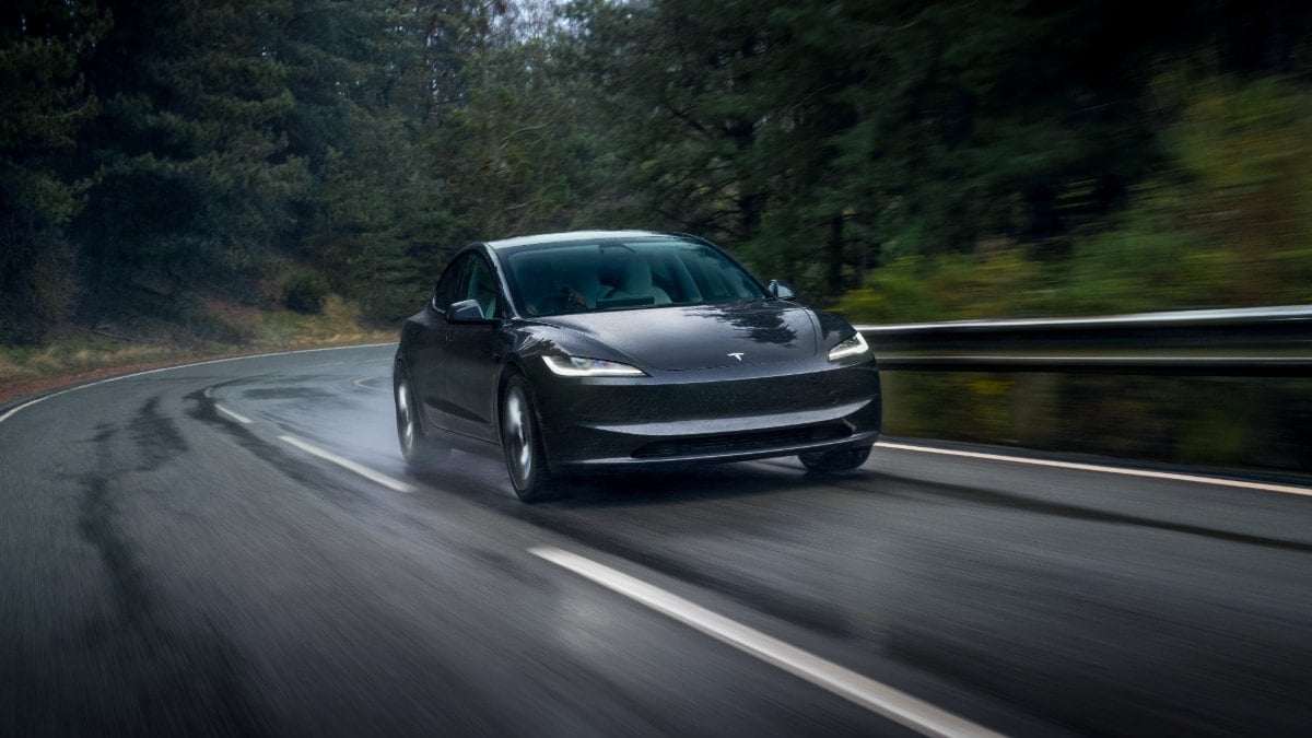Black Tesla Model 3 driving on curved mountain road with motion blur effect