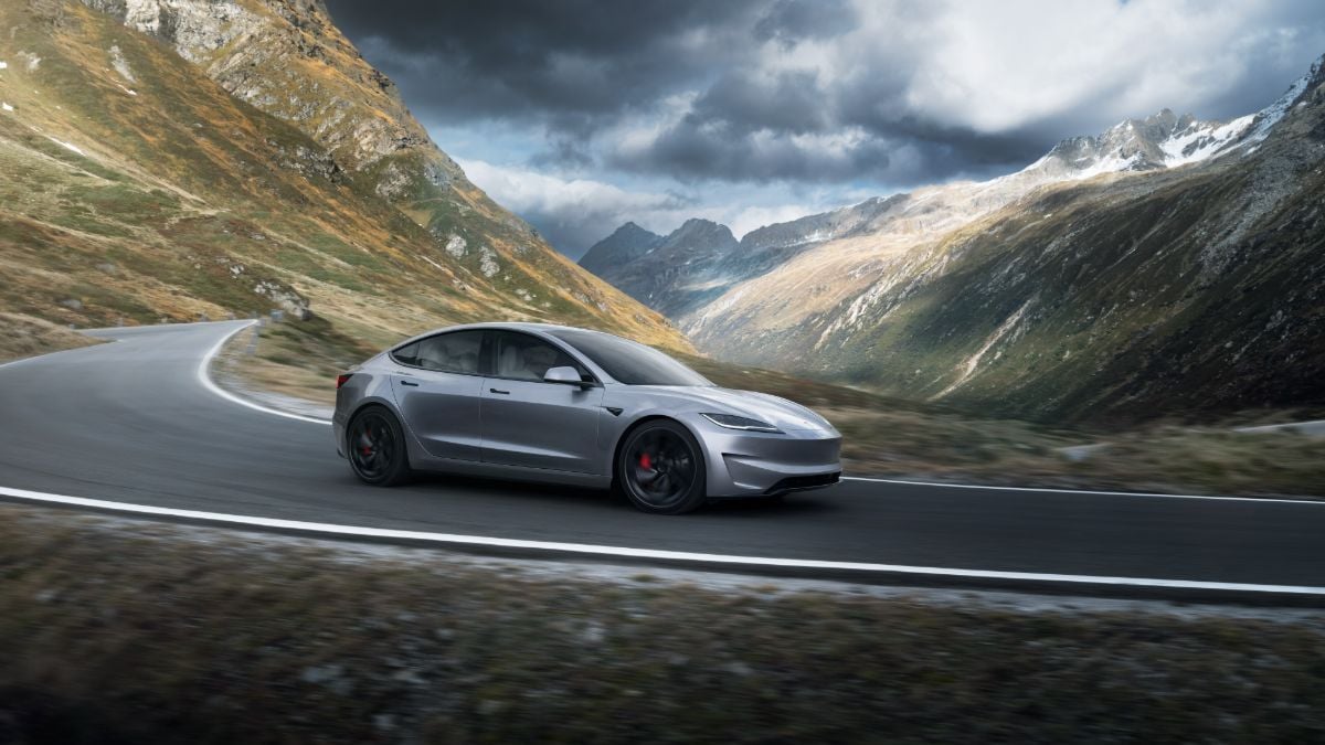 Silver Tesla Model 3 driving on winding mountain road beneath dramatic stormy skies