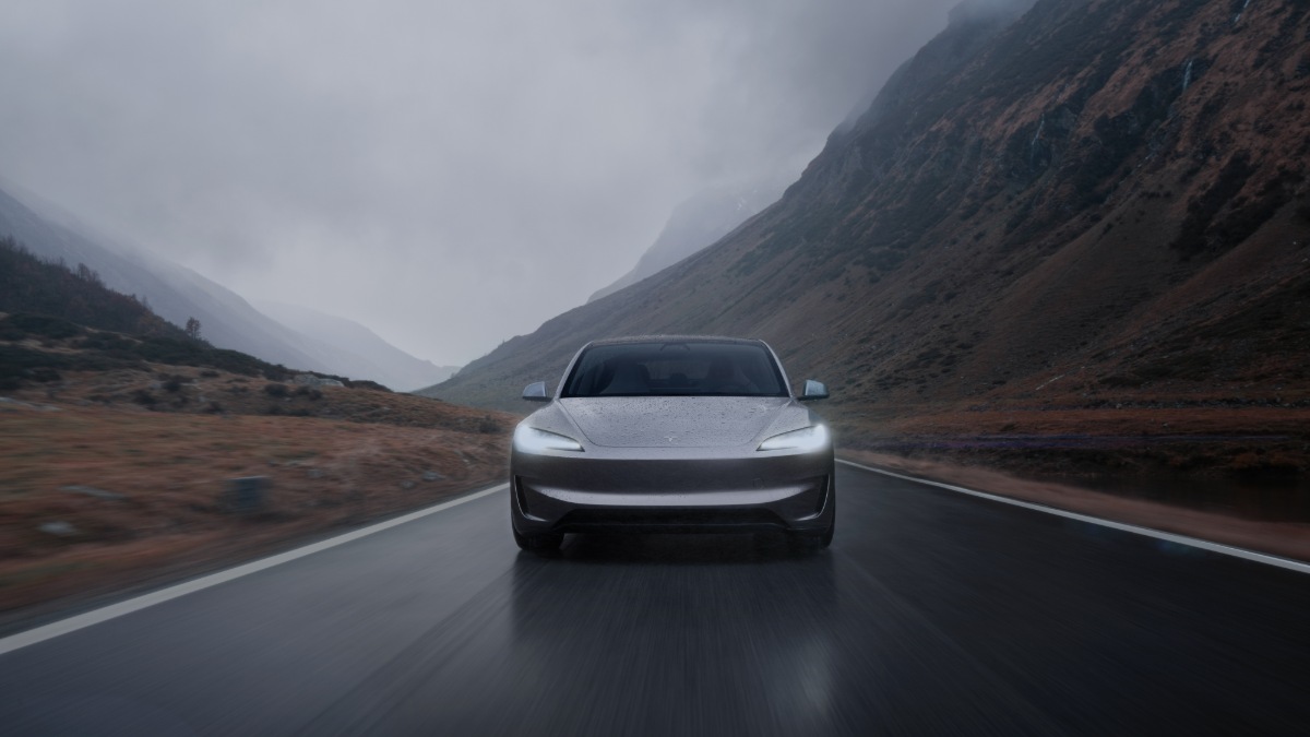 Silver Tesla Model 3 driving on mountain road through misty Scottish Highlands landscape