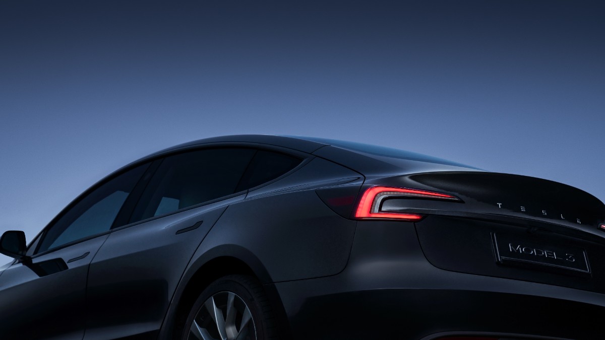 Sleek black Tesla Model 3 with illuminated red tail light against twilight blue sky