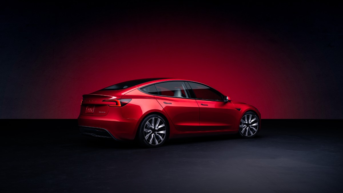 A red Tesla Model 3 is showcased from the side against a dramatic dark and red gradient background.