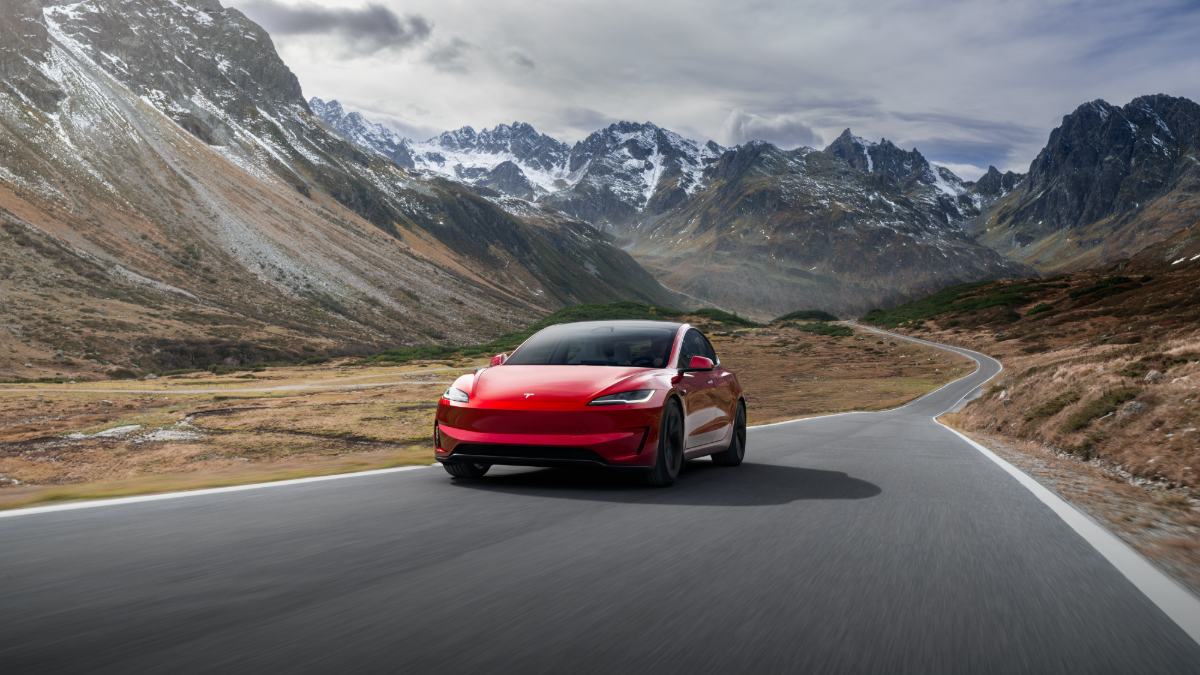 Red Tesla Model 3 driving on winding mountain road with snow-capped peaks in background