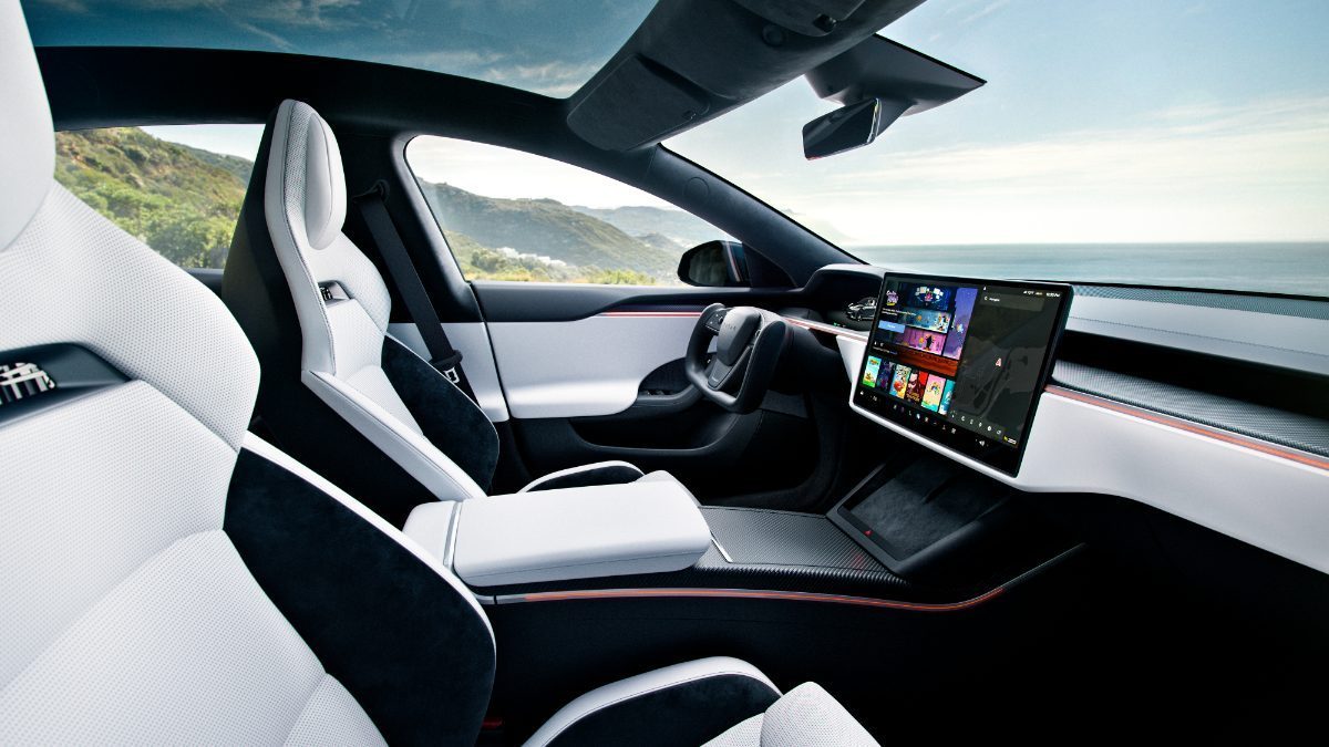 Futuristic car interior with white seats, large touchscreen display, and scenic ocean view.