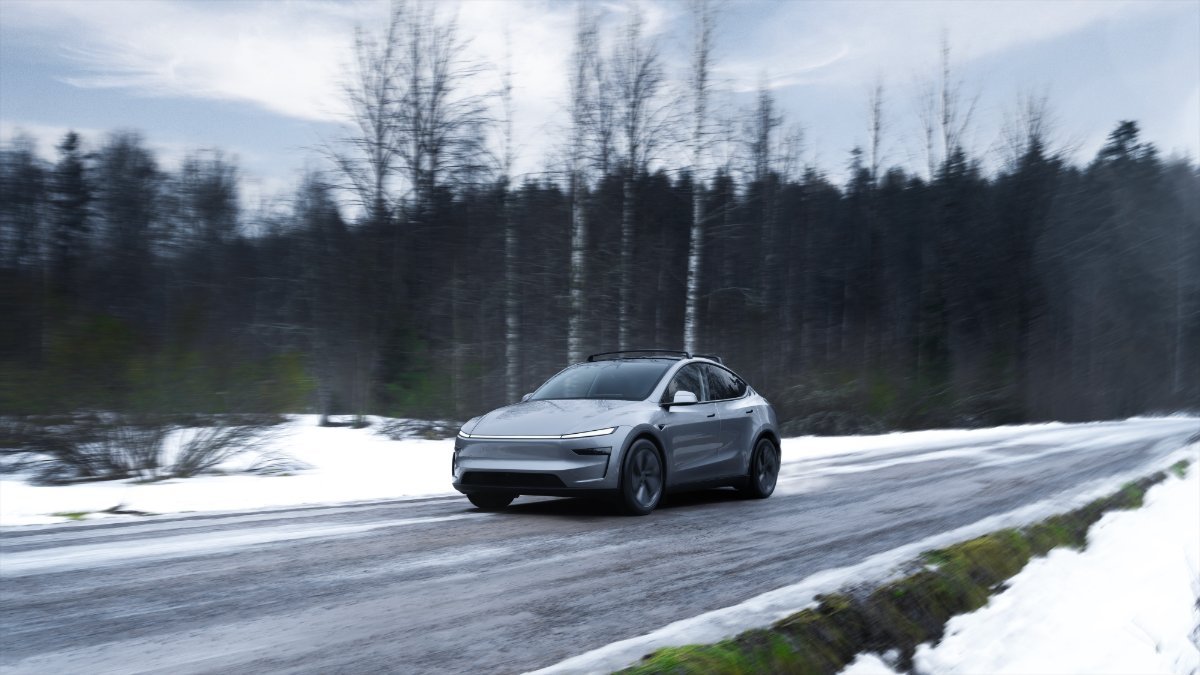 Silver 2026 Tesla Model Y Juniper driving on snowy forest road, sleek electric SUV in motion with winter landscape background