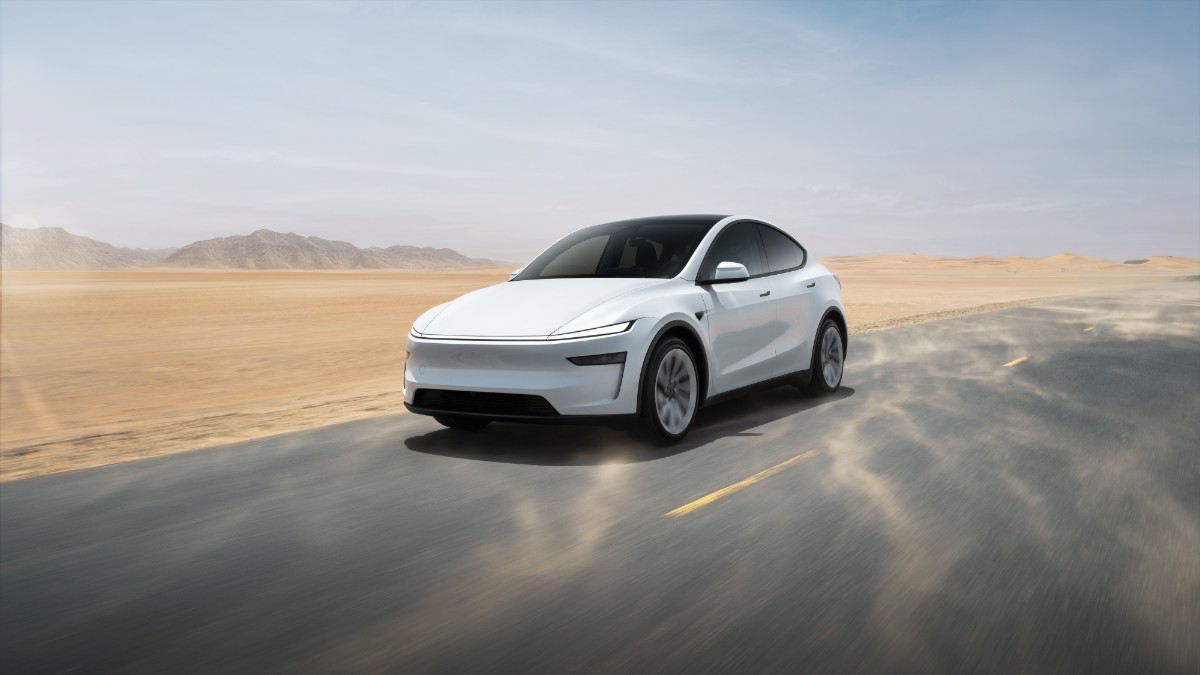2025 Tesla Model Y in white shown from rear three-quarter view on a winding road at sunset, emphasizing sleek EV design.