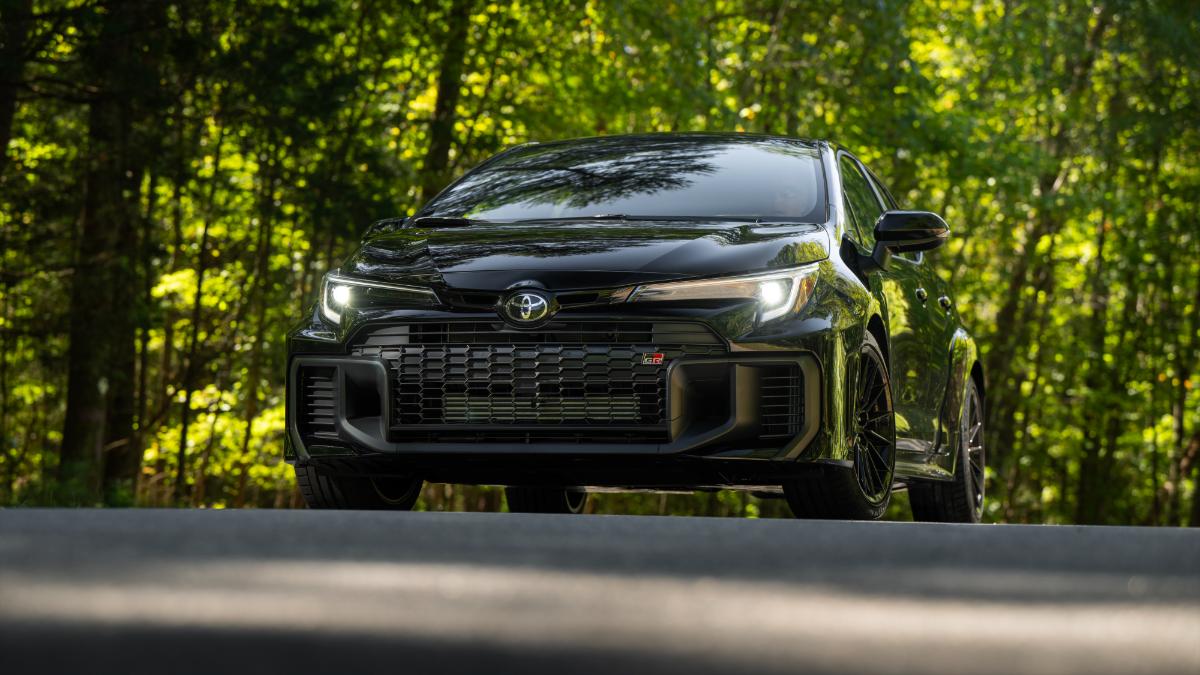 Black 2025 Toyota GR Corolla hatchback parked on woodland road, aggressive stance with dark multi-spoke wheels