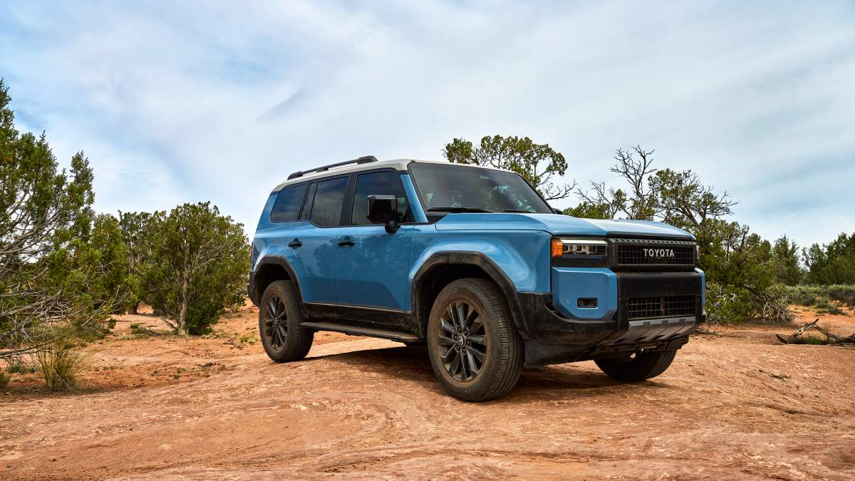 Blue 2025 Toyota Land Cruiser 250 Series photographed from the front three-quarter angle under a cloudy sky in an outdoor landscape.