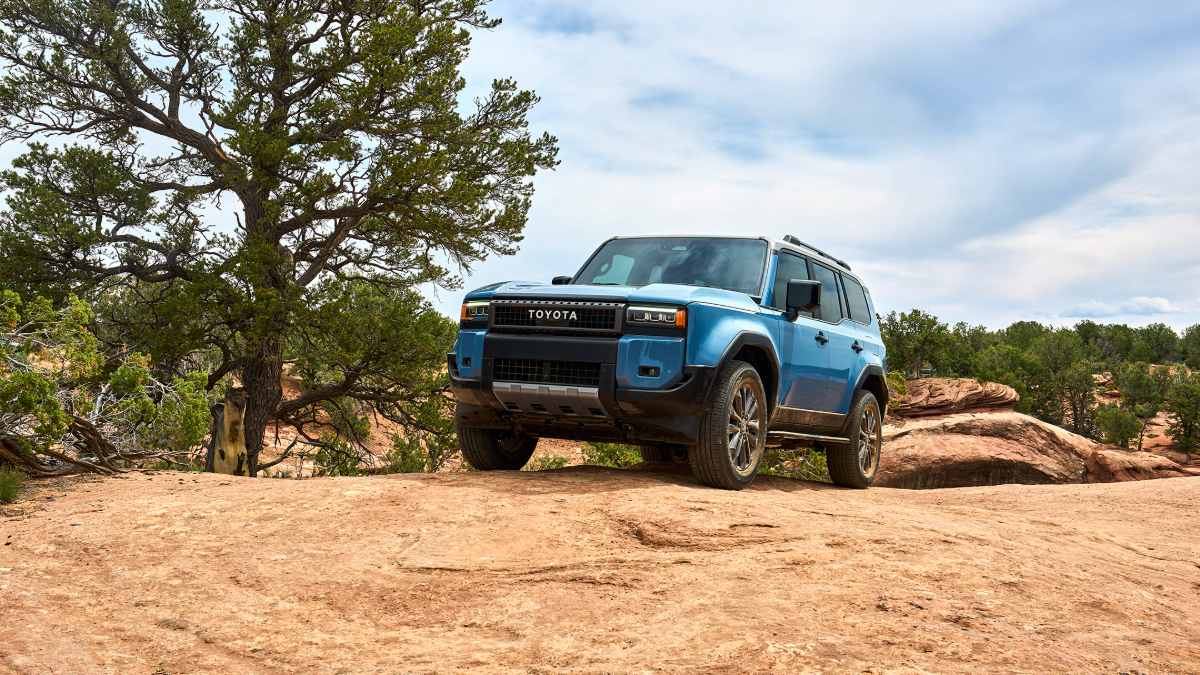 Low-angle front three-quarter view of a blue 2025 Toyota Land Cruiser showcasing rugged suspension and off-road capability.