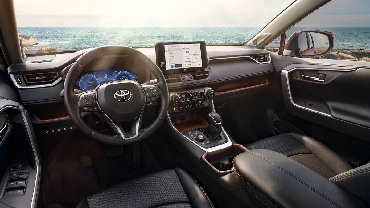 Toyota RAV4 interior with black leather seats, a modern dashboard, and a central touchscreen. The image shows an ocean view through the windshield, conveying a serene tone.