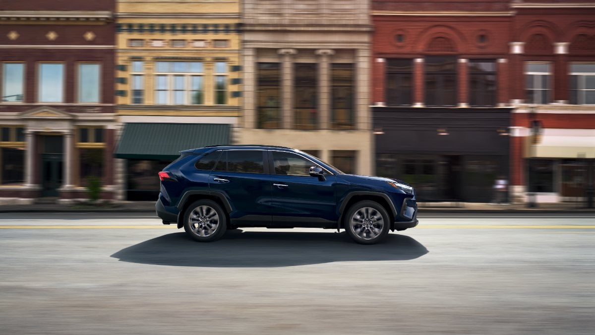 A side profile view of a 2025 Toyota RAV4 in blue, showcasing the vehicle's sleek silhouette and aerodynamic body lines.