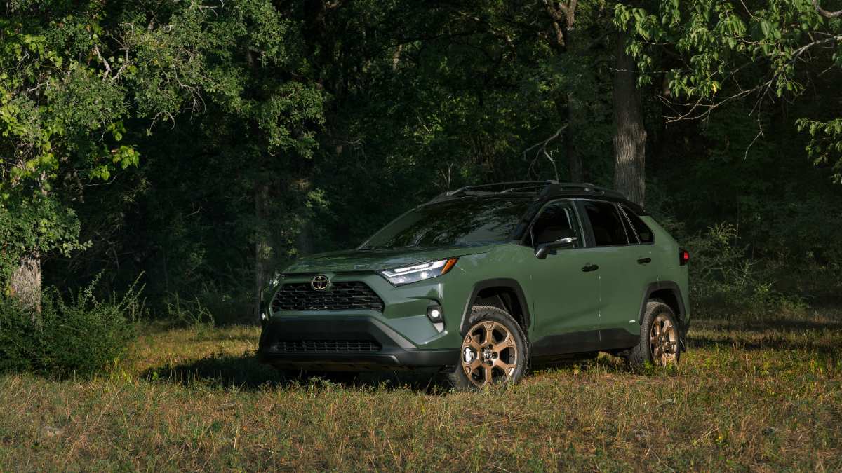 2024 Toyota RAV4 in Army Green, shown at three-quarter front angle, parked in wooded area with bronze wheels and black roof rails.
