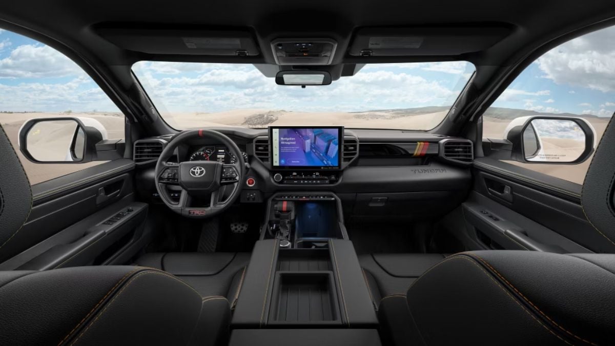 Interior of a 2025 Toyota Tundra with a sleek dashboard. A touchscreen display shows digital features. Panoramic desert view visible through windows conveying adventure.