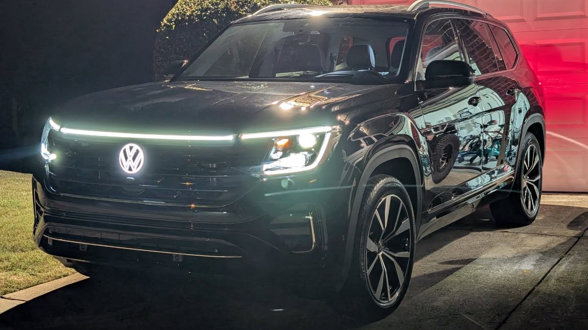 Black Volkswagen SUV with illuminated front lights, parked on a driveway at night.