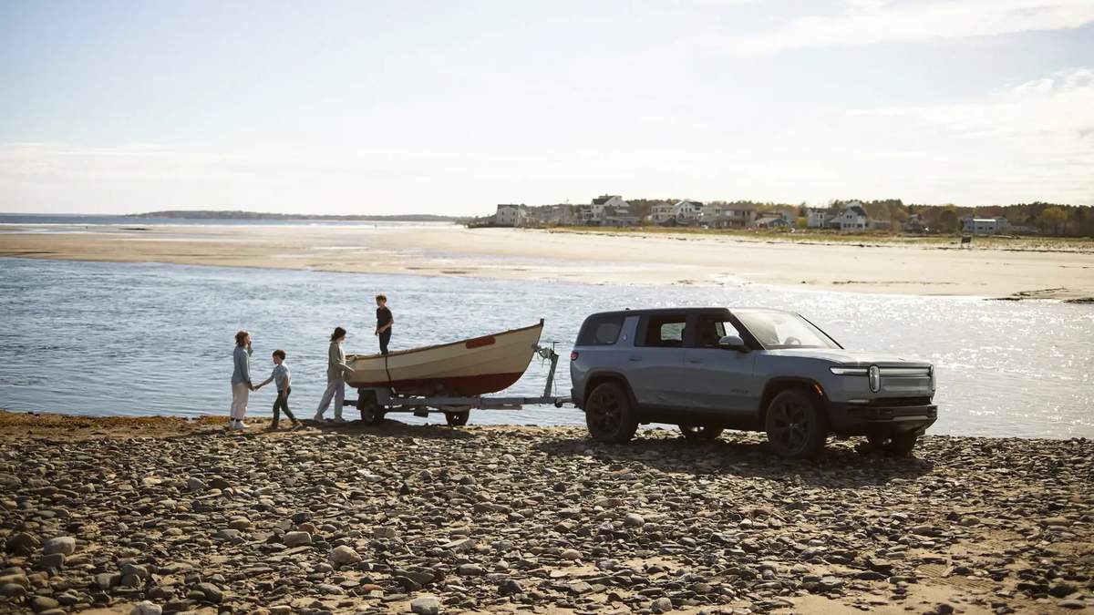 Rivian R1S towing a small boat on a rocky beach shoreline, showcasing electric SUV towing capability