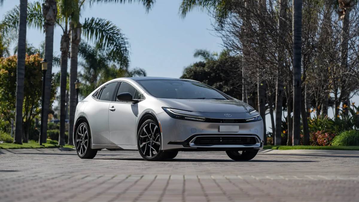 2025 Toyota Prius Prime in silver parked on a paved area surrounded by tall palm trees and tropical landscaping.