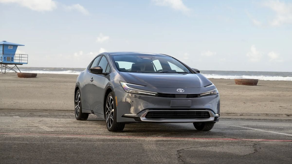 Gray 2025 Toyota Prius parked near a beach with ocean and lifeguard tower in the background, highlighting modern hybrid sedan design.