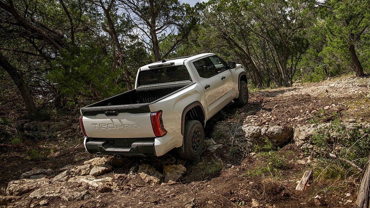 Super White 2025 Toyota Tundra TRD Pro climbing a rocky wooded trail in a rear three-quarter view.