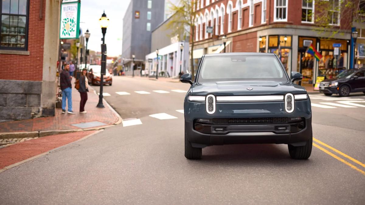 Front view of a Rivian R1S electric SUV driving on a city street, highlighting the signature vertical LED headlights and wide stance.