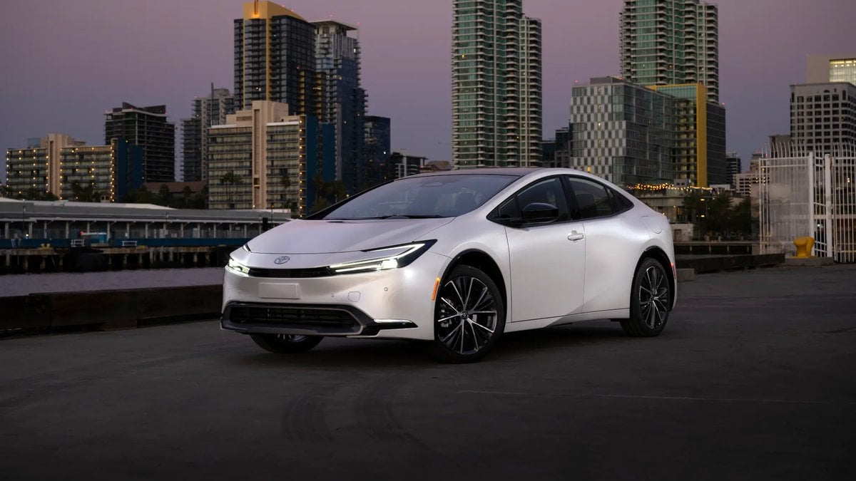 2025 Toyota Prius Limited in Wind Chill Pearl parked on a pier with a city skyline in the background at dusk.