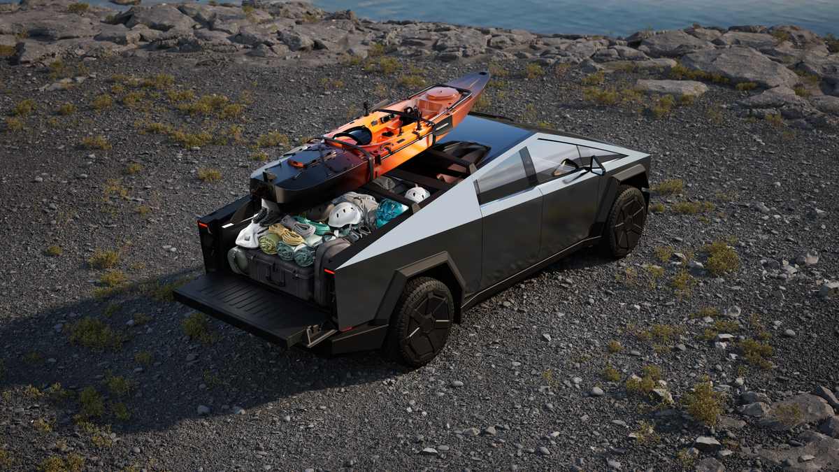 Tesla Cybertruck stainless steel pickup with open truck bed loaded with camping and kayaking gear, including an orange kayak, parked on rocky terrain near water.