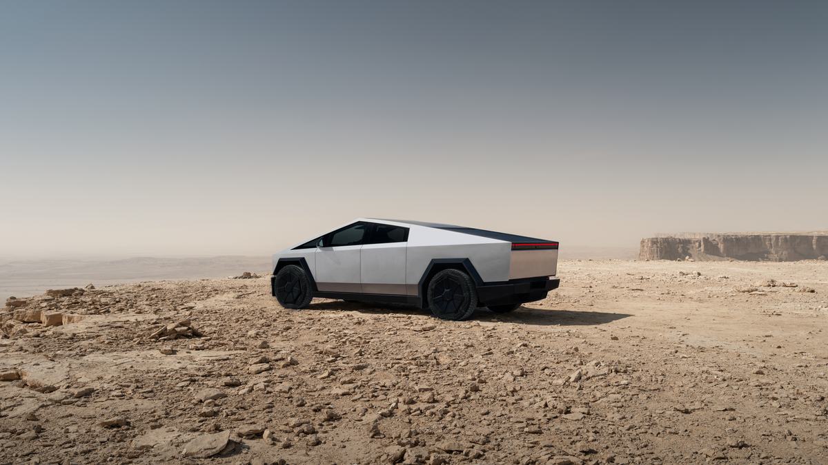 Tesla Cybertruck parked on a rocky desert plateau, wide rear view highlighting stainless steel body and futuristic electric pickup design