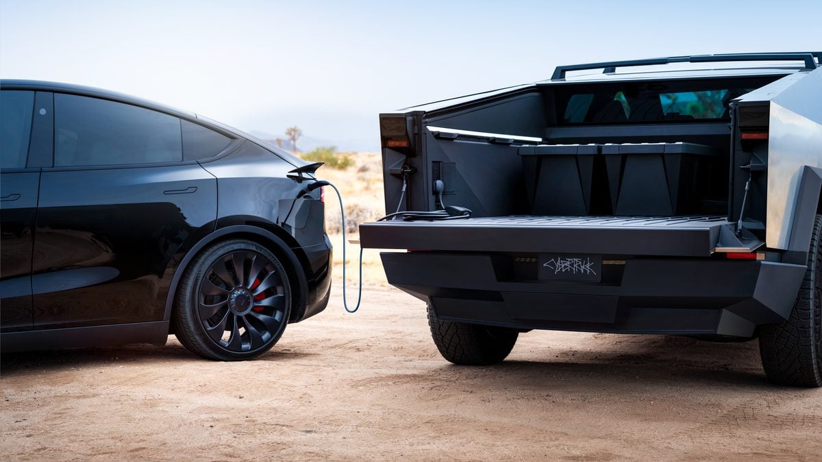Tesla Model S charging from a Cybertruck with the stainless steel tailgate open, showing the Cybertruck’s rear bed and integrated power setup in a desert setting.