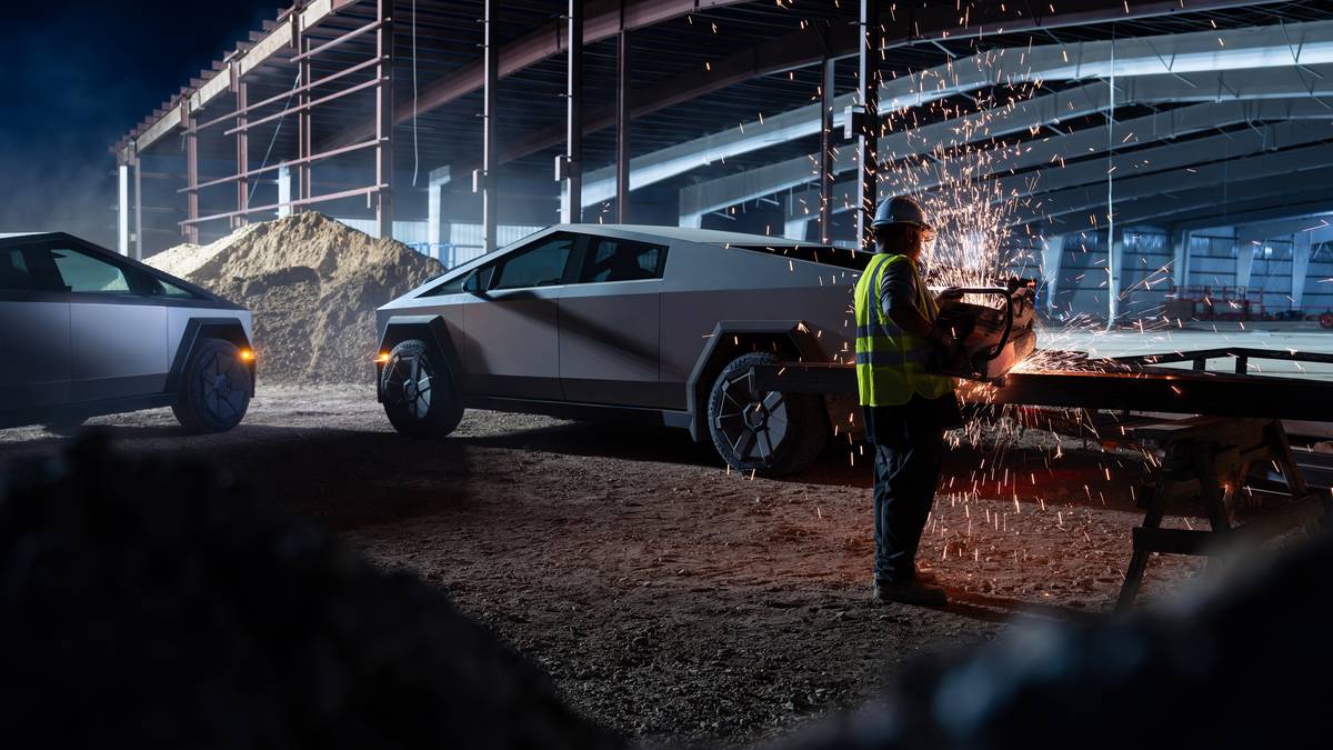 Tesla Cybertruck parked at a construction site at night while a worker cuts metal, illustrating industrial durability and worksite use.