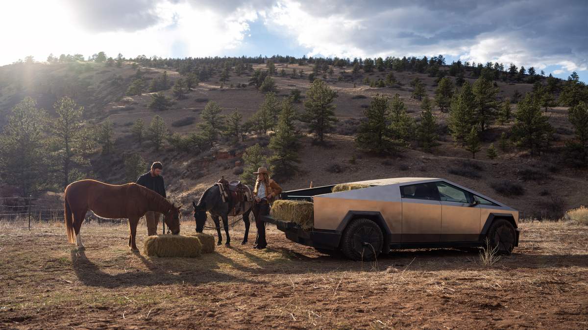 Tesla Cybertruck at a ranch near horses and hay bales in a rural field