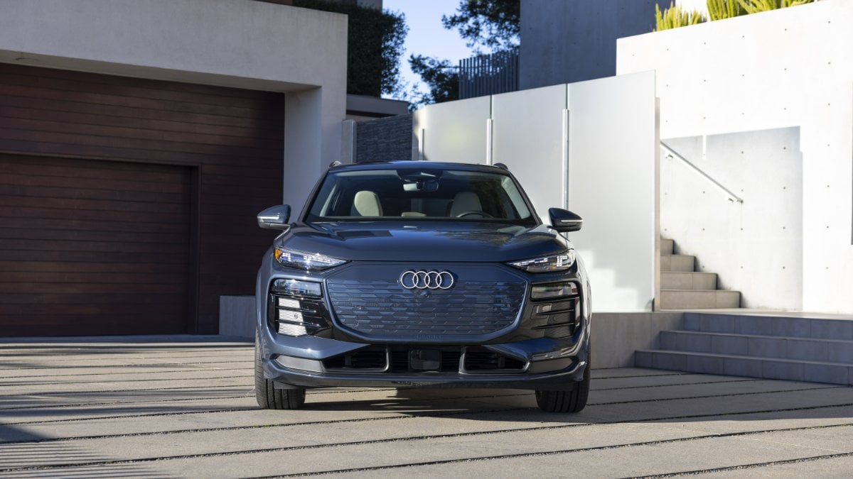 2024 Audi Q4 e-tron in metallic blue, front three-quarter view, showcasing distinctive LED headlights and closed grille, parked on modern concrete steps.