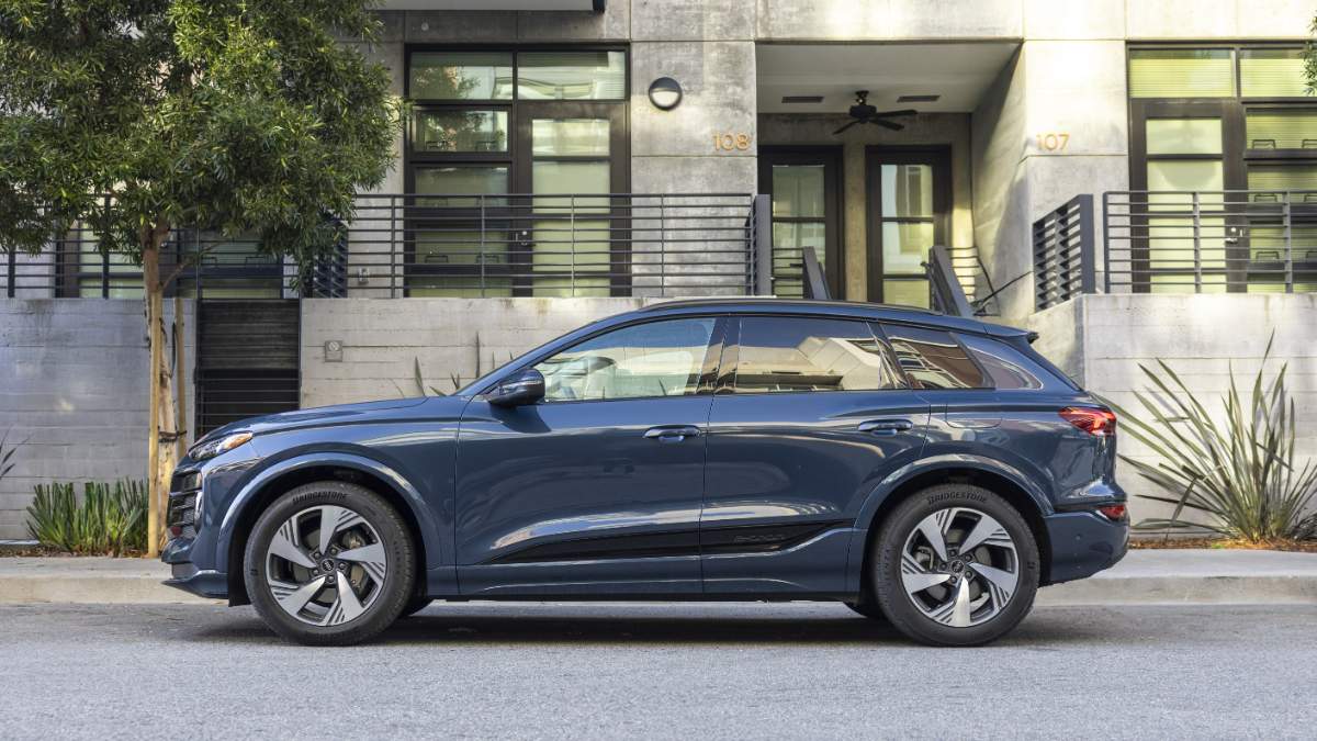 2024 Audi Q6 e-tron in deep blue, side profile view, featuring distinctive alloy wheels and chrome trim, parked outside modern apartment building.