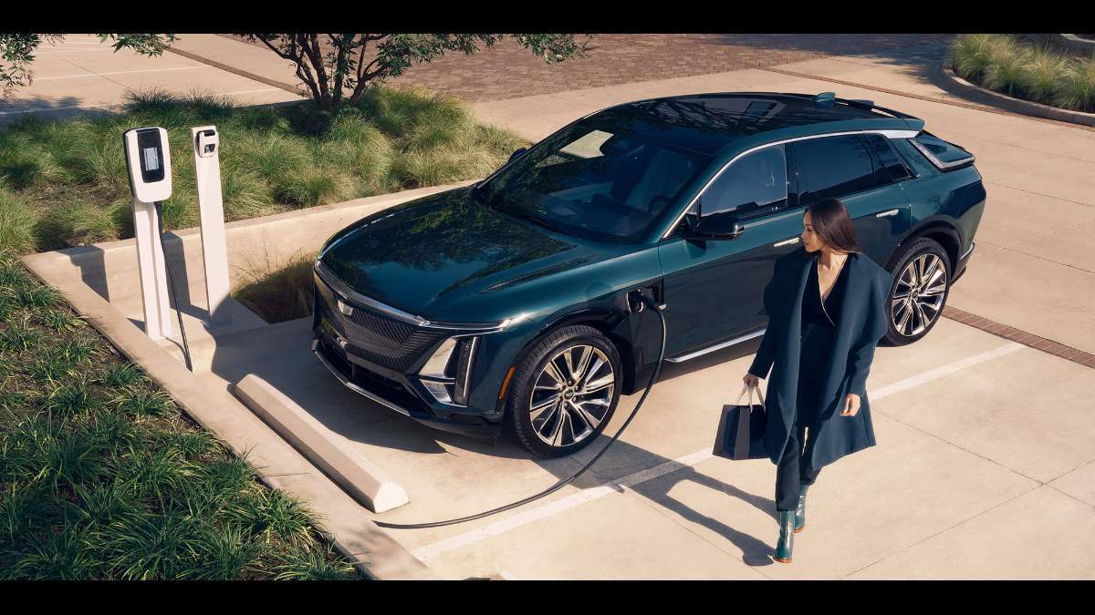 2026 Cadillac Lyriq in dark green, front three-quarter view, charging at an electric station with distinctive grille and wheels.