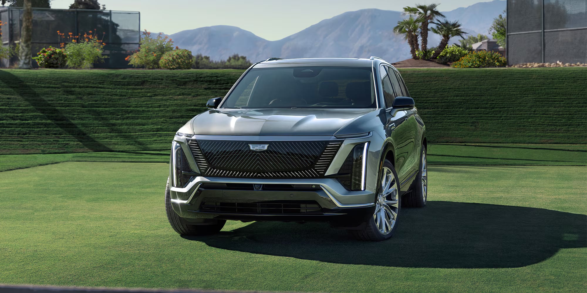 A sleek gray 2026 Cadillac Vistiq parked on a manicured lawn with mountains in the background, highlighting its modern design.
