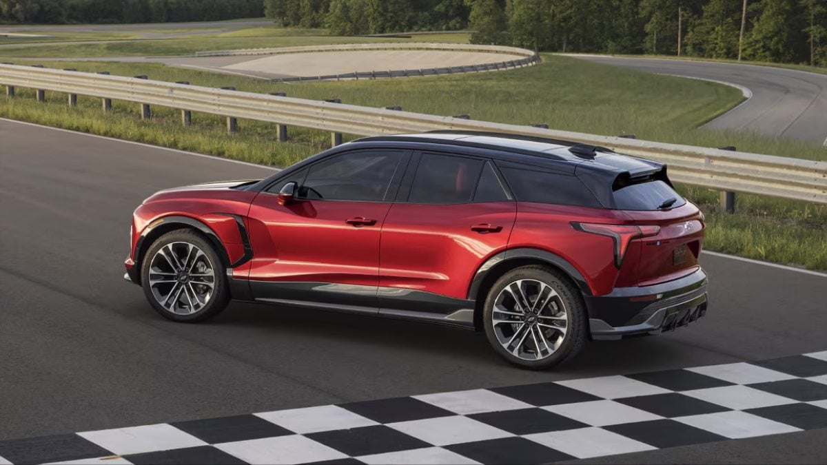 A sleek red SUV with black accents, parked at a racetrack near a checkered finish line, surrounded by green fields and curves.