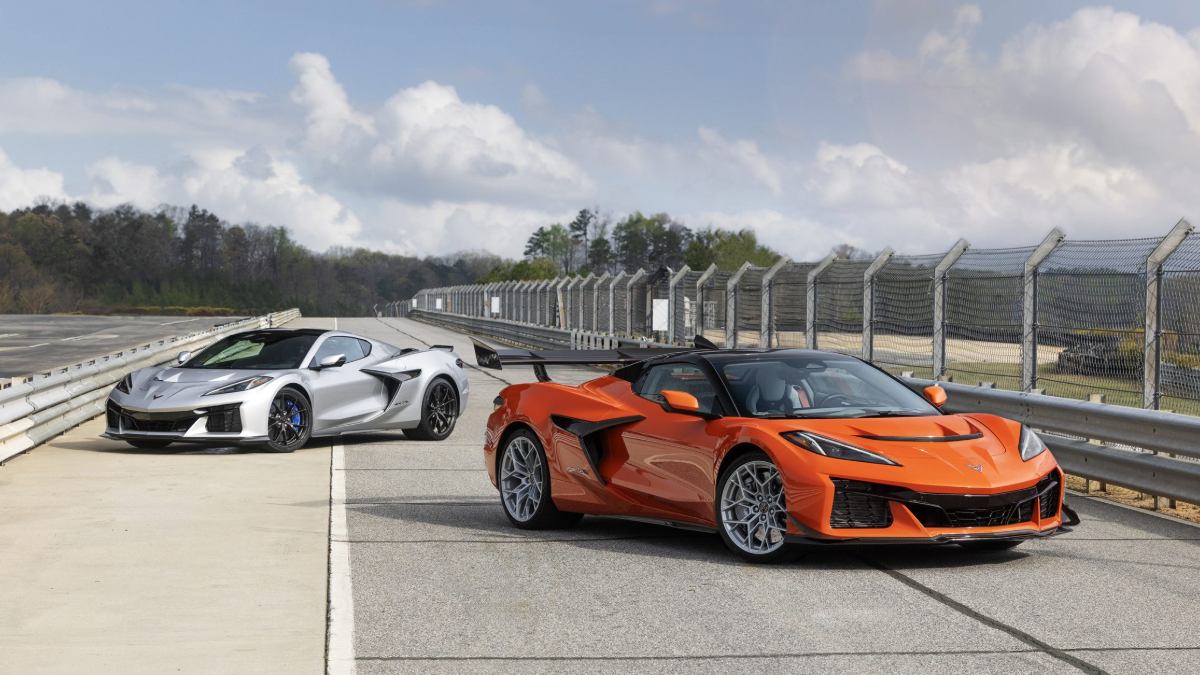 An orange 2026 Chevrolet Corvette and a silver 2026 Chevrolet Corvette parked at what appears to be a race track, both shown from a three-quarter front view with dramatic styling and aerodynamic features visible.