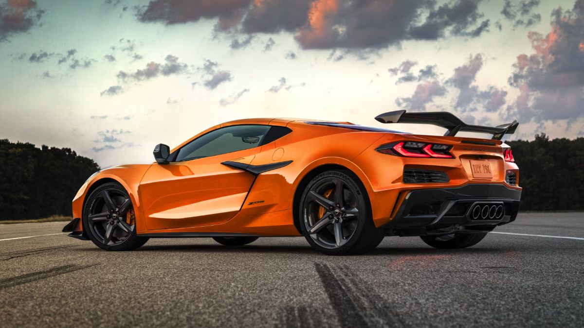 Orange sports car parked on a road with a cloudy sky background.