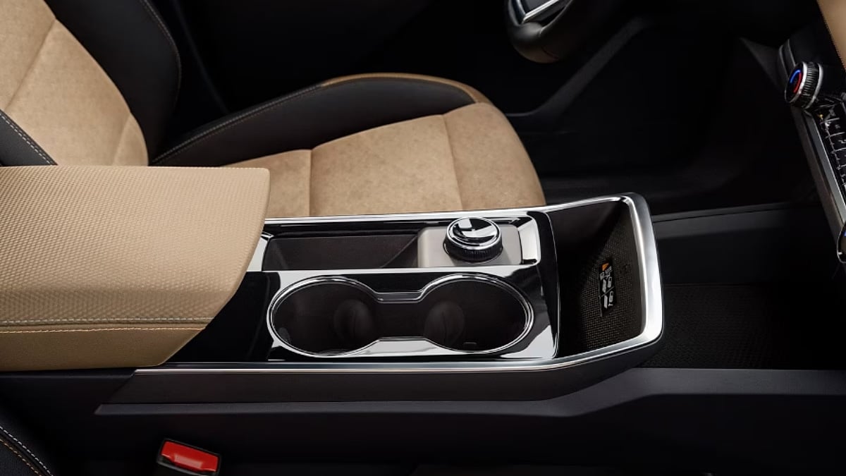 Close-up of a beige leather armrest inside a 2026 Chevrolet Equinox EV and black center console with chrome accents, featuring dual cup holders and a rotary control knob.