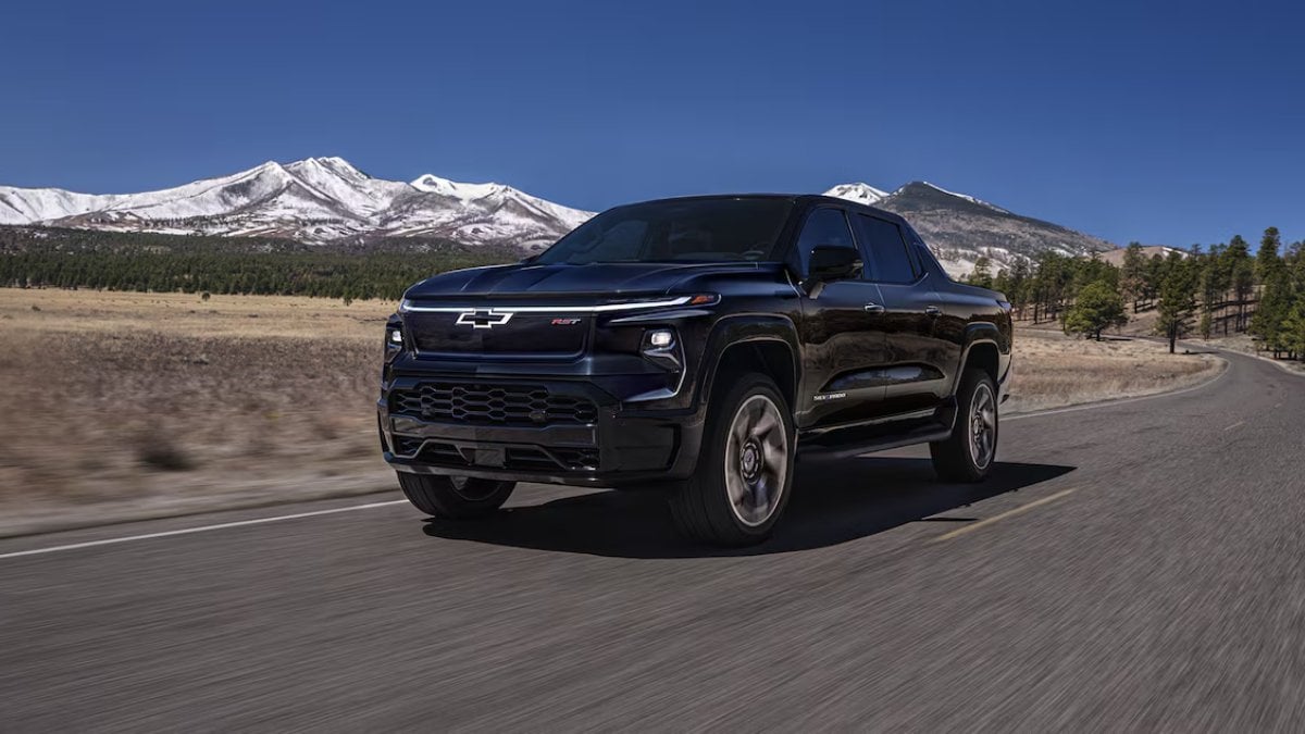 Black pickup truck driving on a road with snow-capped mountains in the background.