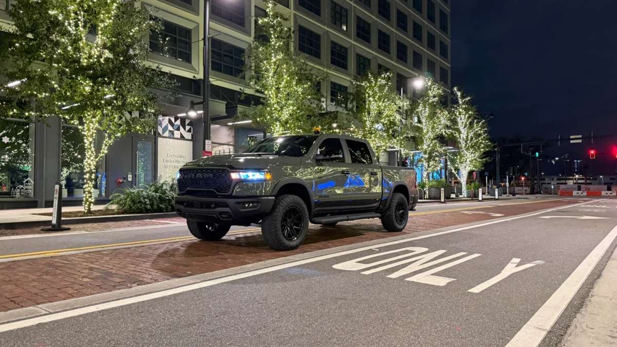 Front three-quarter view of a lifted green 2026 Dodge Ram truck driving through a modern downtown street at night