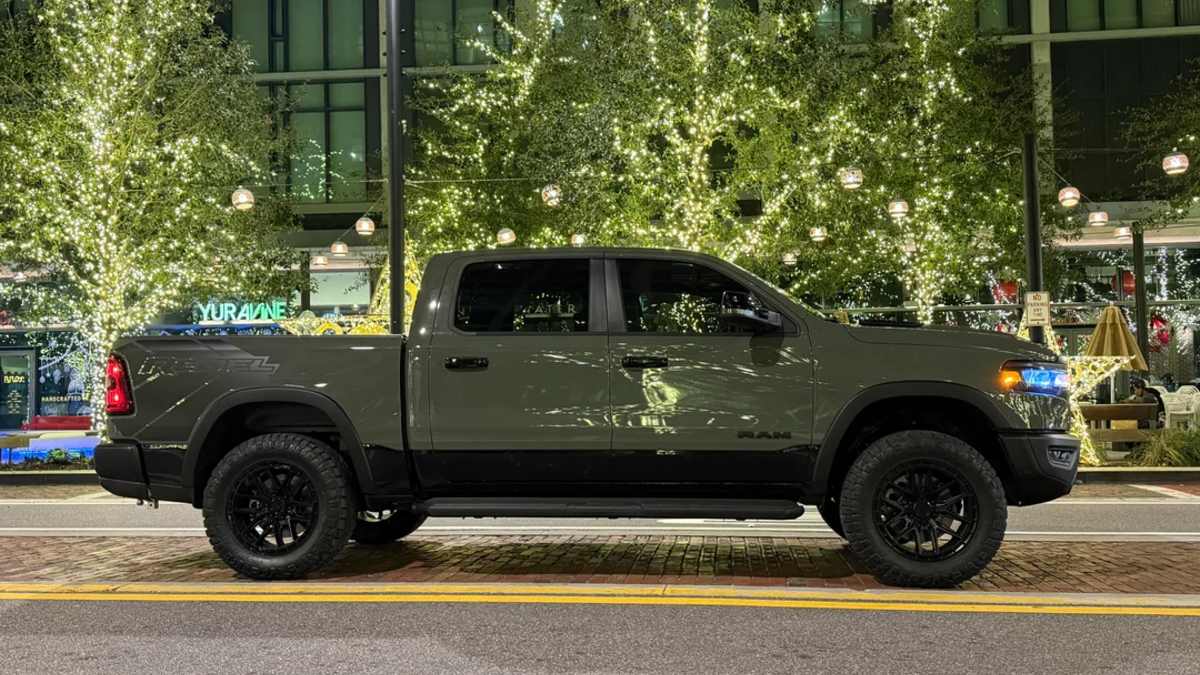 Side profile of a green 2026 Dodge Ram pickup truck with off-road tires parked on an urban street at night