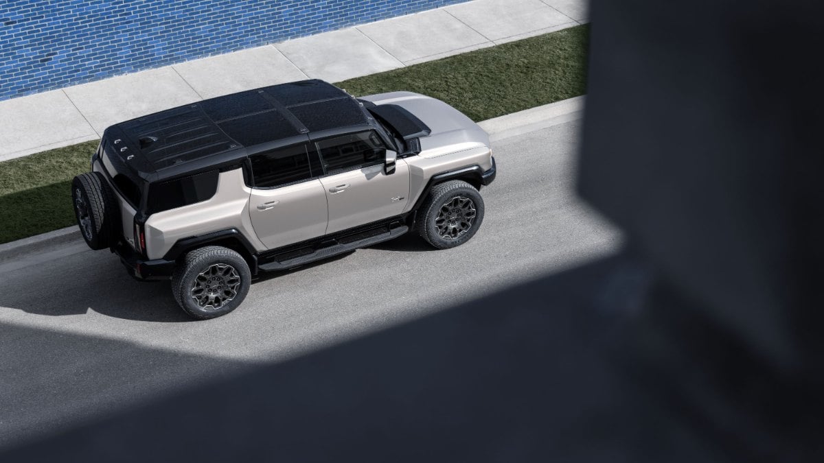 A beige SUV with a black roof parked on a street beside a blue wall.