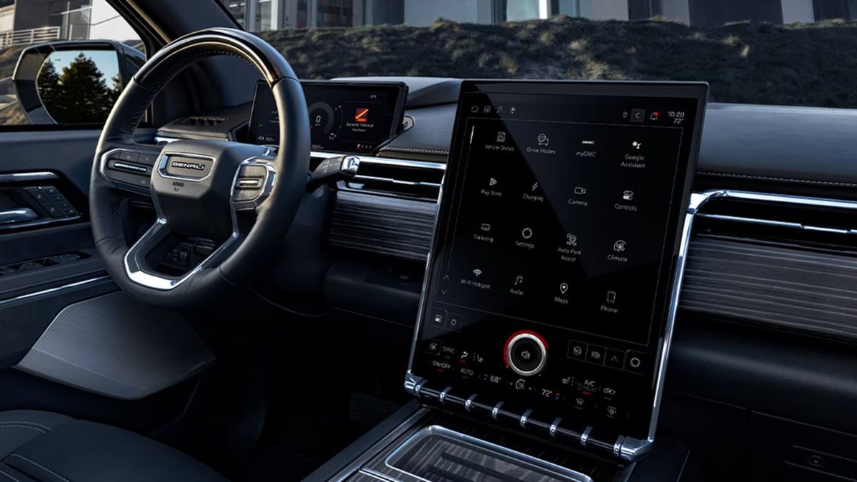 A 2026 GMC Sierra EV's interior featuring a sleek, modern steering wheel and large touchscreen display with icons. Dark leather seats exude comfort and sophistication.