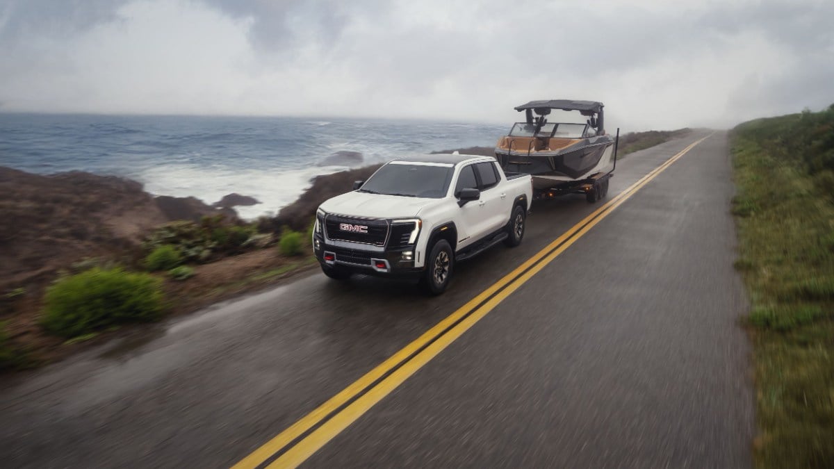 White pickup truck towing a boat on a coastal road with ocean in background.