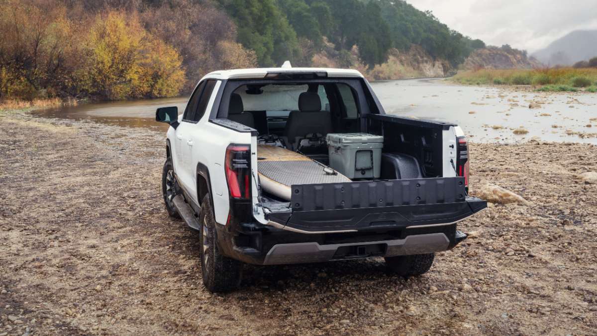 White pickup truck with open tailgate parked by a river, carrying gear and equipment.