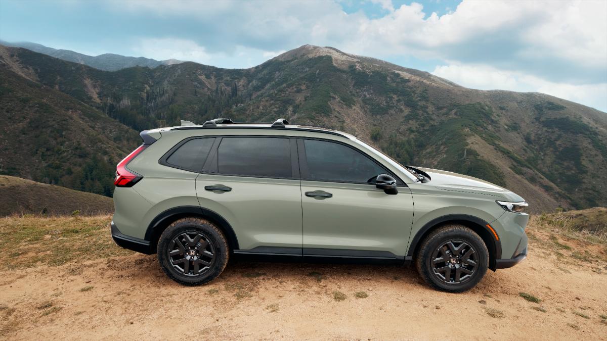 Light sage green Honda CR-V crossover SUV parked on dirt trail with rugged mountain landscape background