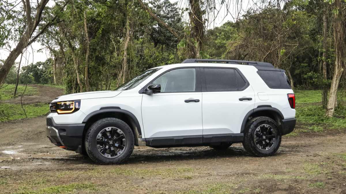 2026 Honda Passport TrailSport in white parked on a dirt path, shown in a front three-quarter view with rugged off-road styling.