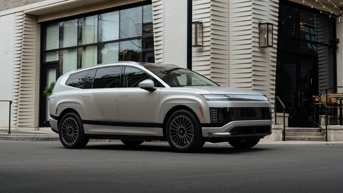 A silver 2026 Hyundai Ioniq 9 viewed from the side profile, showcasing its luxurious modern design and distinctive multi-spoke black wheels against an urban architectural backdrop.