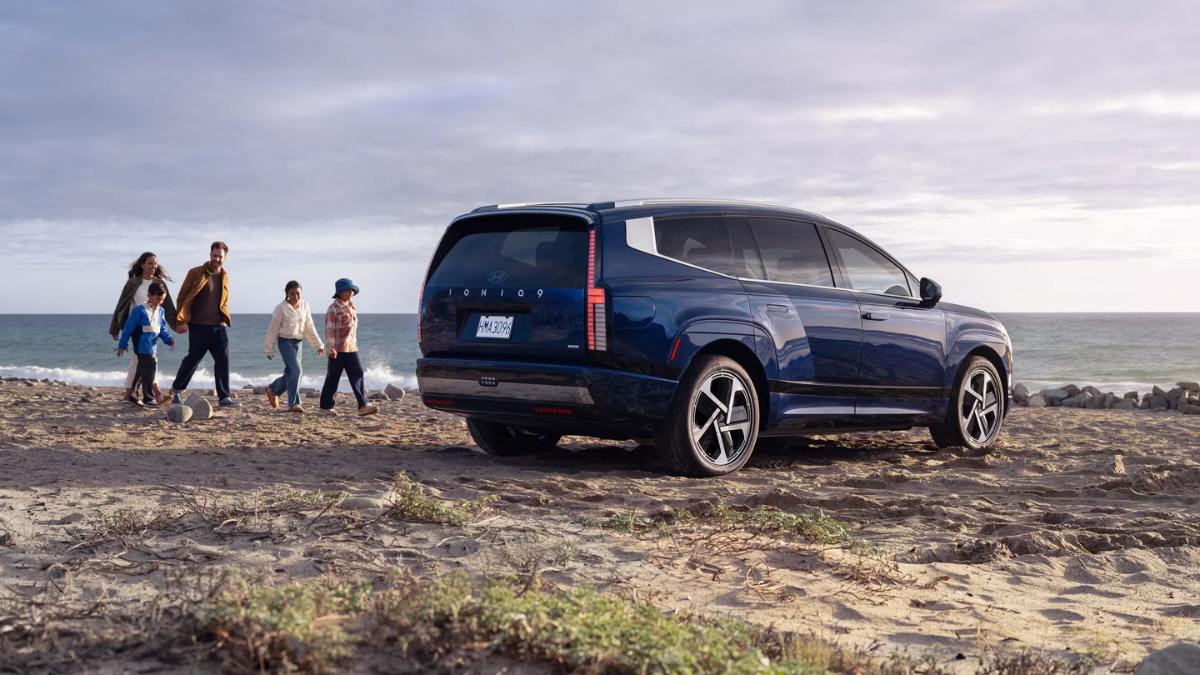Blue Hyundai Ioniq SUV parked on beach while group walks along shoreline at dusk